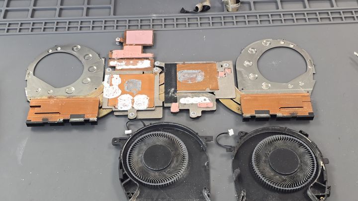 Disassembled laptop with fans, heatsinks and cooling parts exposed